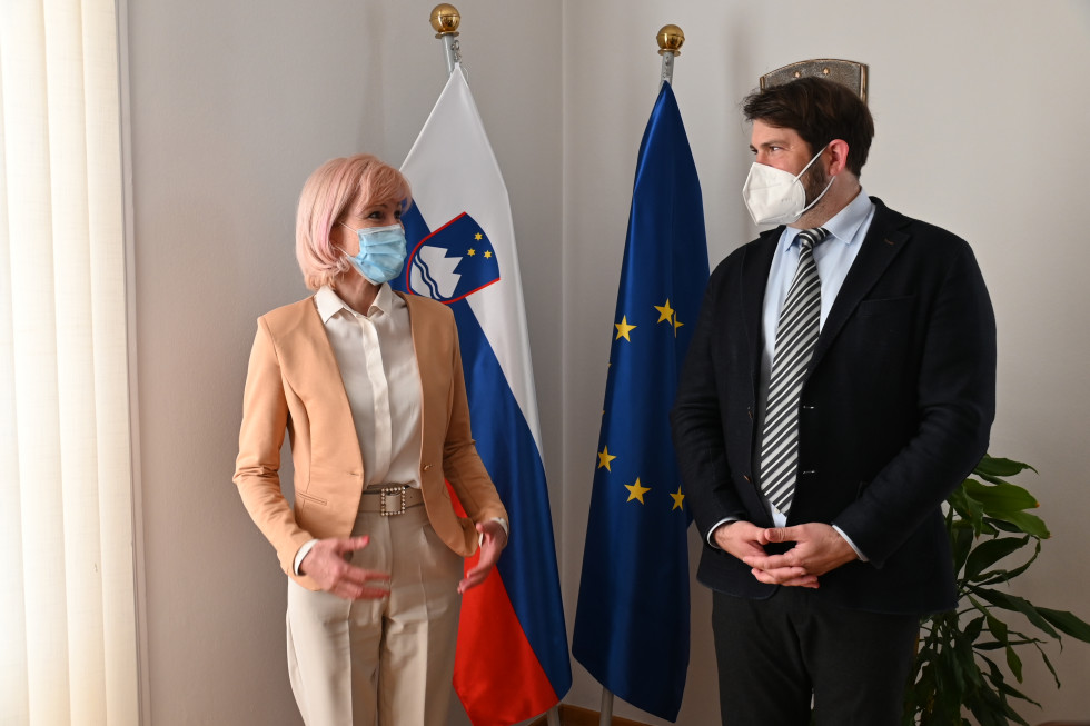 Ministrica in zagovornik načela enakosti stojita pred slovensko in evropsko zastavo v ministričini pisarni