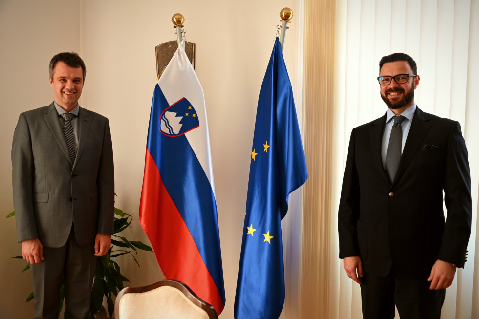 Minister in veleposlanik na fotografiji pred slovensko in evropsko zastavo v pisarni ministra