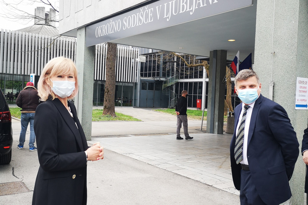 Ministrica Kozlovič stoji na levi strani slike, pred dvorano nad Gospodarskem razstavišču. Na desni strani stoji predsednik Okrožnega sodišča v Ljubljani Marko Pogačnik