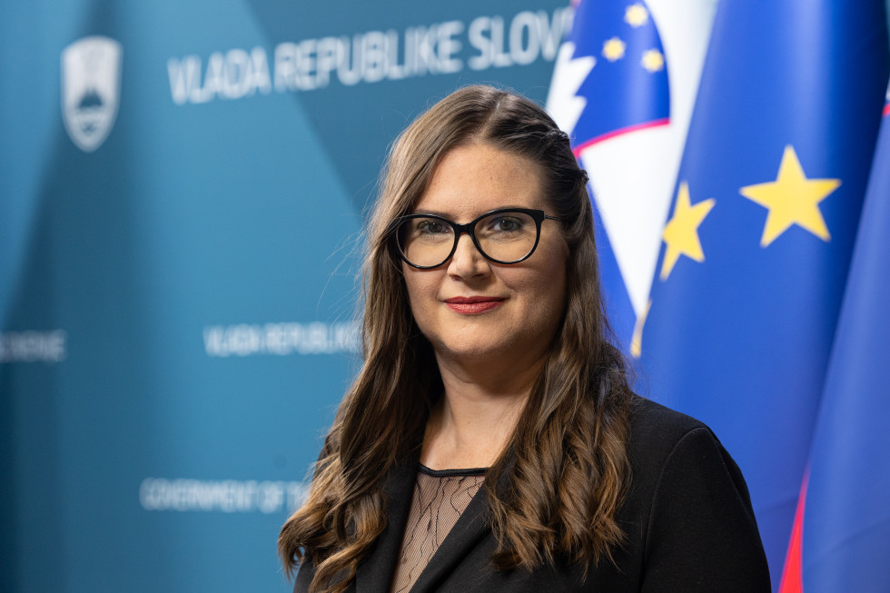 Potret ministrice. Zadaj slovenska in zastava Evropske unije.