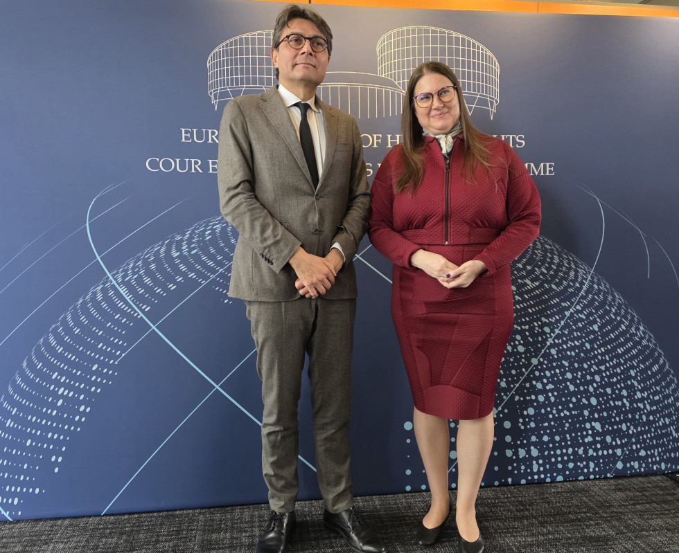 Moški in ženska stojita eden zraven drugega. Za njima temno moder pano.