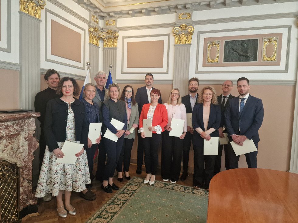 Skupinska fotografija po zaprisegi sodnih izvedencev in sodnih cenilcev na Ministrstvu za pravosodje. V sejni sobi stoji enajst zapriseženih sodnih izvedencev in cenilcev skupaj z državno sekretarko dr. Majo Čarni Pretnar.
