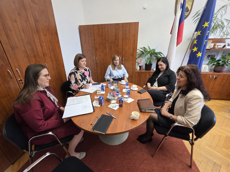 Sestanek ministrice za pravosodje s predstavnicami sodišča v pisarni; udeleženke sedijo za mizo in razpravljajo ob dokumentih.