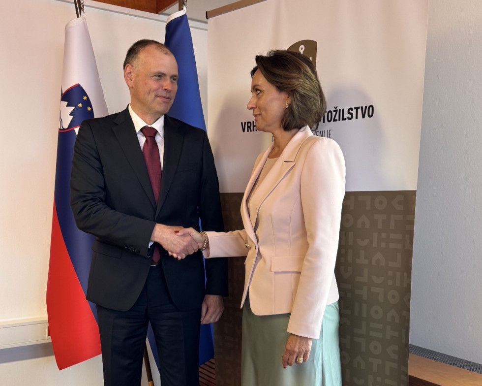Minister za pravosodje Mihael Zupančič in generalna državna tožilka dr. Katarina Bergant se rokujeta pred slovenskima zastavama in panojem Vrhovnega državnega tožilstva Republike Slovenije.
