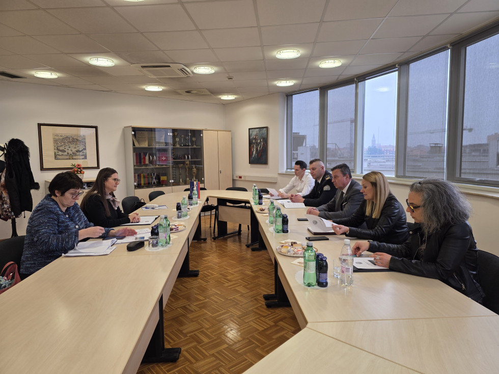 Vodstvo koperskega zapora in ministrica sedijo za veliko ovalno mizo v sejni sobi.