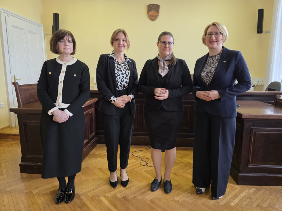 Ministrica za pravosodje mag. Andreja Kokalj stoji s predstavnicami sodišča v sodni dvorani pred sodniškim pultom.