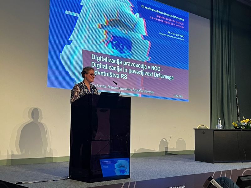 Ženska govori za govorniškim pultom ob projekciji predstavitve na zaslonu.