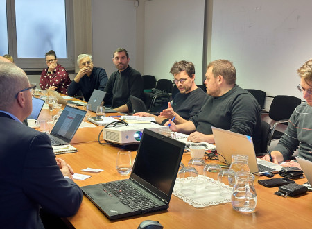 Člani in članice sveta sedijo za mizo, na njej prenosni računalniki in dokumenti