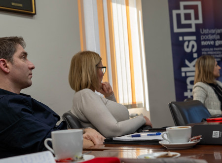 Udeleženci sedijo za mizo in poslušajo predavanje