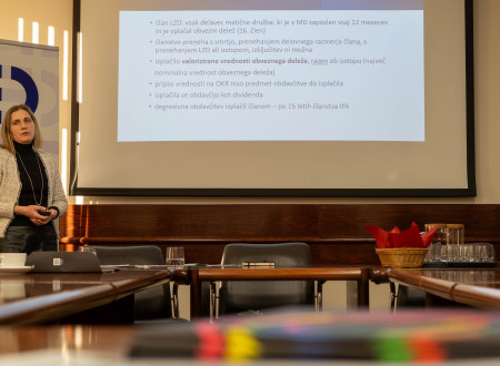 Leja Drofenik Štibelj za govorniškim odrom, levo platno, spredaj udeleženci dogodka