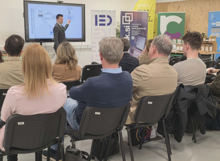 Tilen Božič pred stoji pred velikim ekranom, spredaj sedijo udeleženci posveta