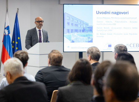 Viceguverner za govorniškim pultom, zadaj prezentacija, pred njim udeleženci konference