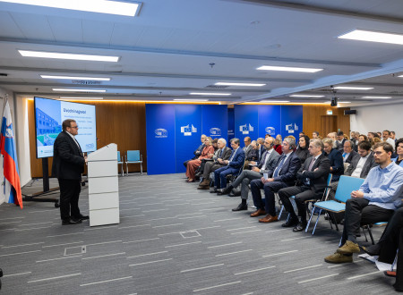 Minister stoji pred govorniškim pultom, pred njim udeleženci konference sedijo na stolih