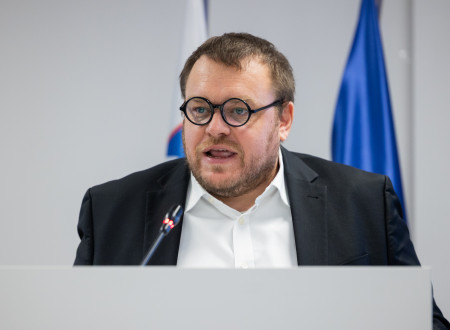 Minister stoji za govorniškim pultom, pred njim mikrofon