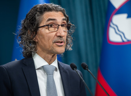 Vodja klicnega centra stoji za govorniškim pultom, zadaj zastave