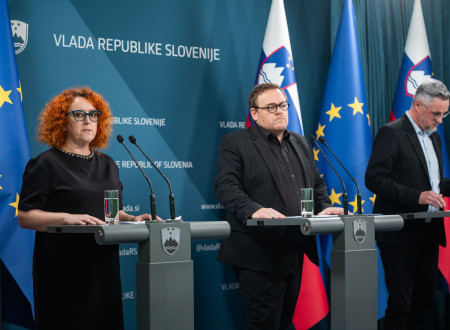 Nastja Belcer Premrl in Simon Maljevac stojita za govorniškim pultom, zadaj zastave