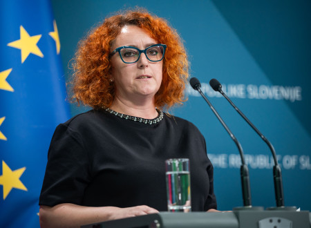 Nastja Belcer Premrl stoji za govorniškim pultom, zadaj zastave