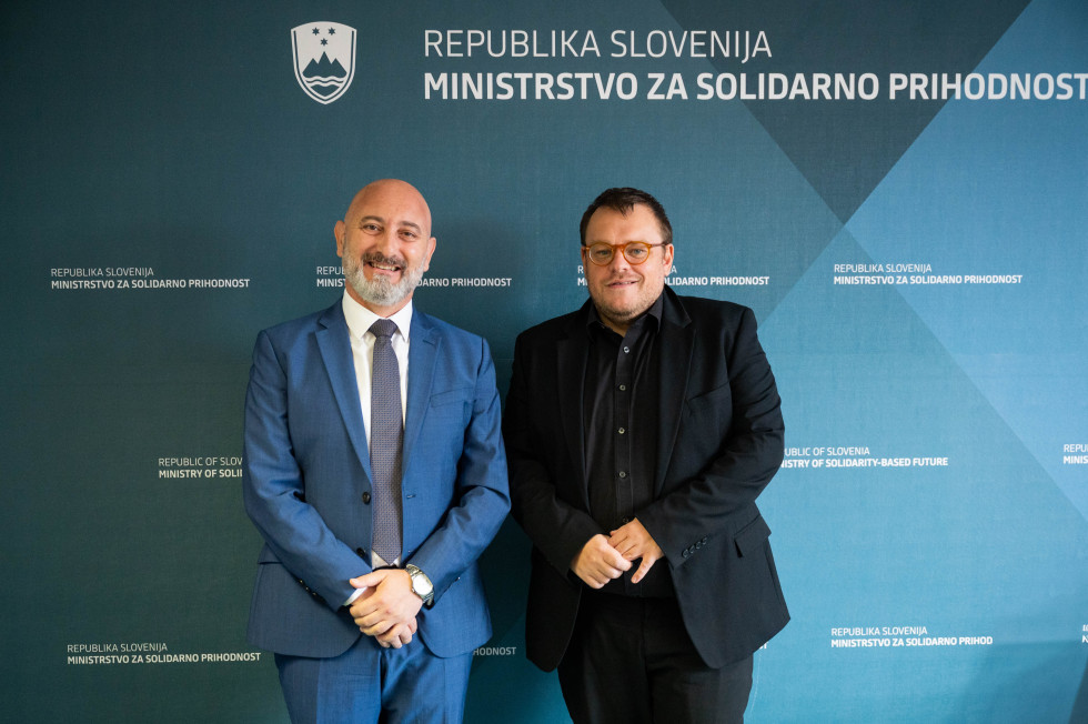 Ministra stojita pred zidom, na katerem piše Republika Slovenija in Ministrstvo za solidarno prihodnost