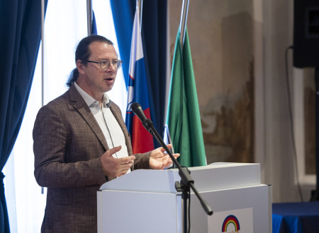 Državni sekretar stoji za govorniškim pultom, zadaj zastave