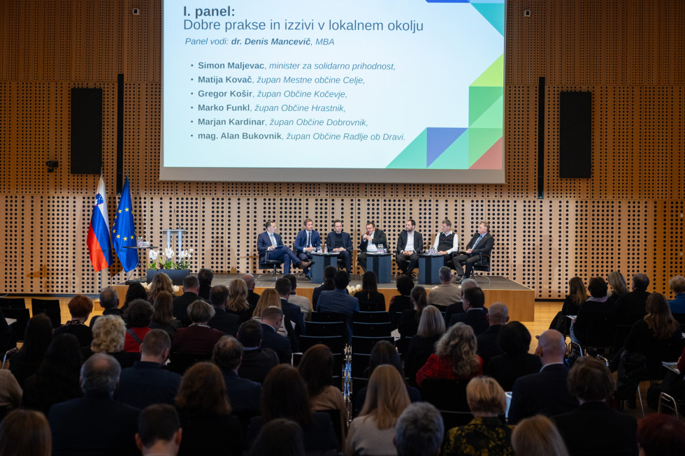 Razprava na panelu. Govorci sedijo na odru. Zadaj na steni je prezentacija.