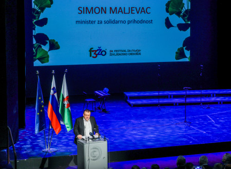 Minister ima nagovor, stoji za govorniškim odrom, za njim zastave