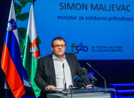 Minister ima nagovor, stoji za govorniškim odrom, za njim zastave