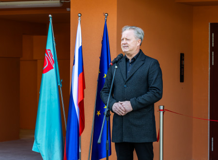 Tribušon ima nagovor, pred njim mikrofon, zadaj zastave