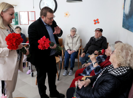 Minister ima v roki rožo, ki jo daje varovanki doma