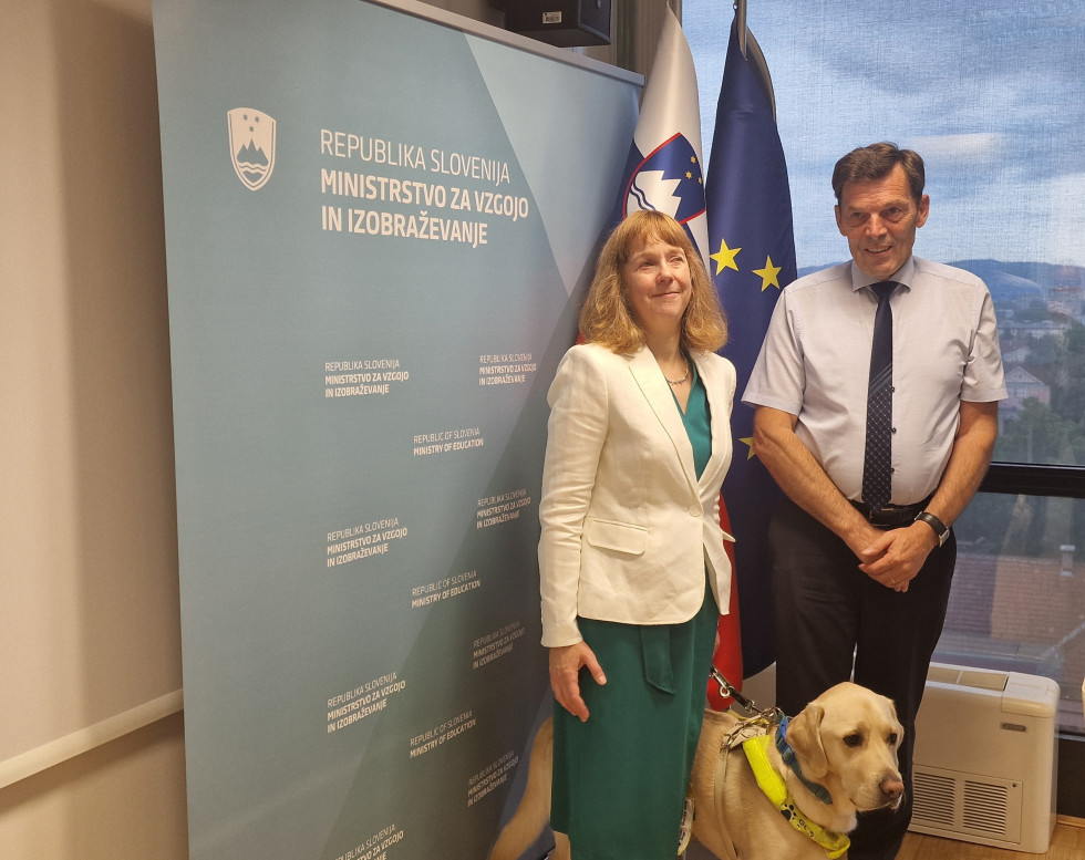Minister Logaj stoji pred panojem z britansko veleposlanico in njenim psom.