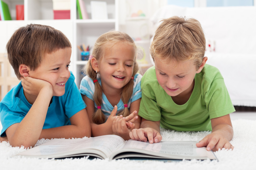 Trije nasmejani otroci berejo knjige.