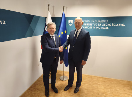 Nekdanji in sedanji minister se rokujeta, v ozadju slovenska in evropska zastava.