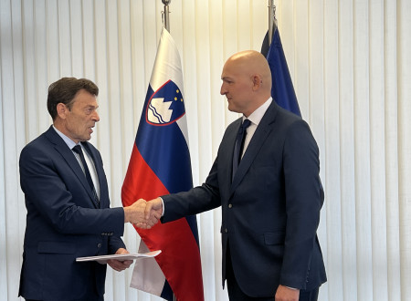Nekdanji in sedanji minister se rokujeta, v ozadju slovenska in evropska zastava.