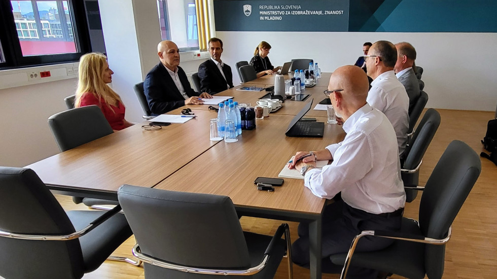 Udeleženci sestanka sedijo za konferenčno mizo v sejni sobi.