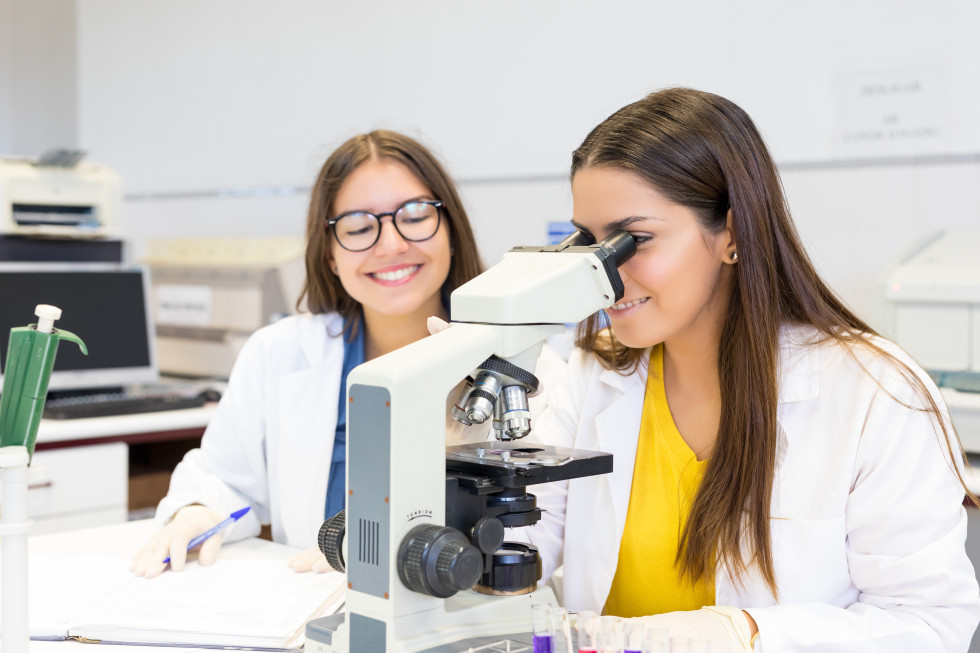 Two young scientists in lab coats working with a microscope in a laboratory.