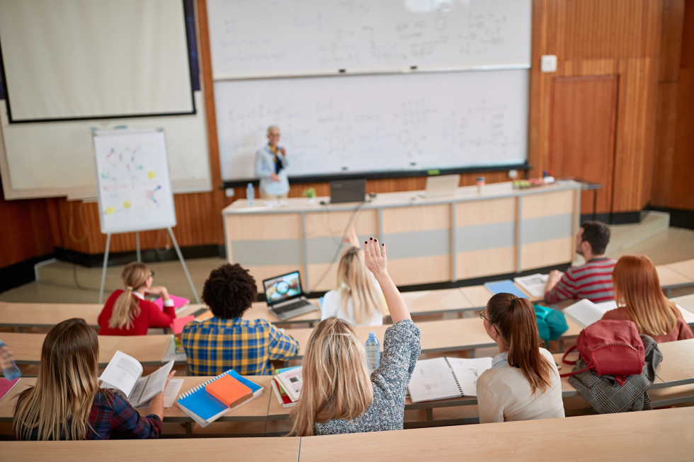 Študentke in študenti v predavalnici, v ozadju profesorica med predavanjem.