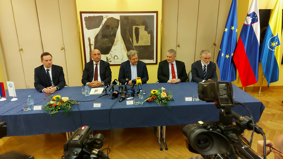 V ospredju dve kameri, v ozadju za mizo sedijo govorci med novinarsko konferenco. 