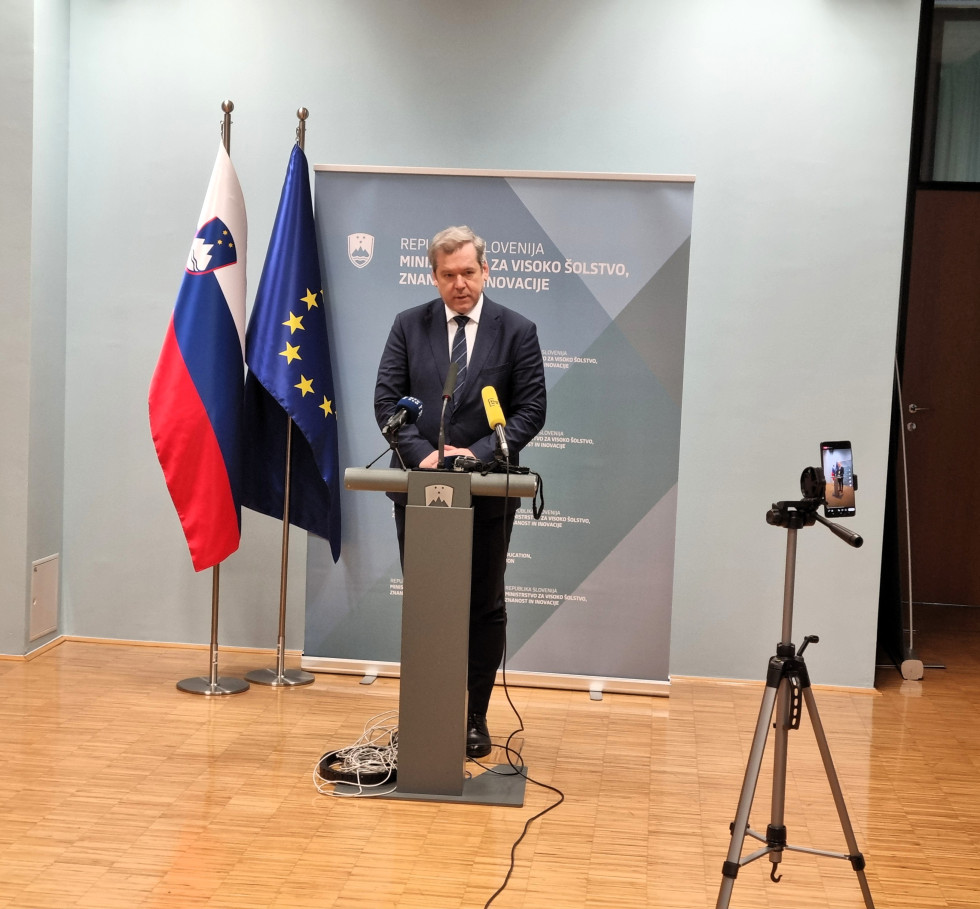 Minister papič za govornico na novinarski konferenci, za njim slovenska in evropska zastava ter pano ministrstva.