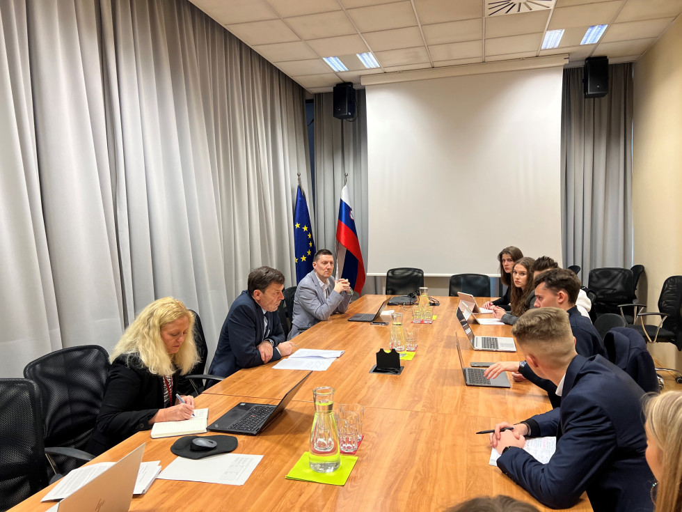 Minister za vzgojo in izobraževanje dr. Vinko Logaj sedi za mizo na sestanku z dijaki.