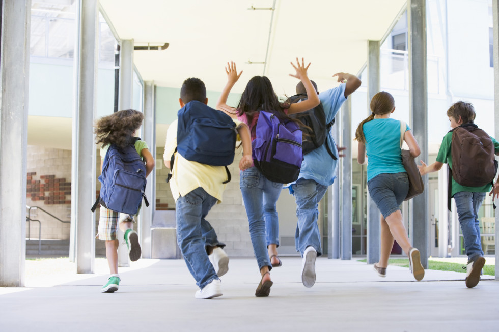 Učenci s šolskimi torbami tečejo na hodniku. 