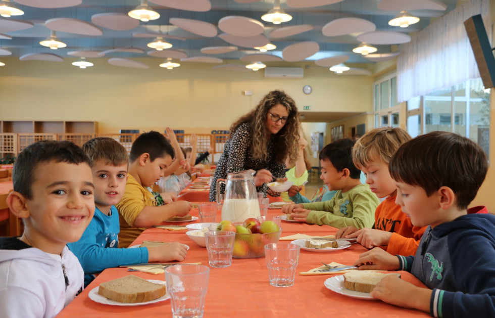 Učiteljica deli zajtrk učenkam in učencem.