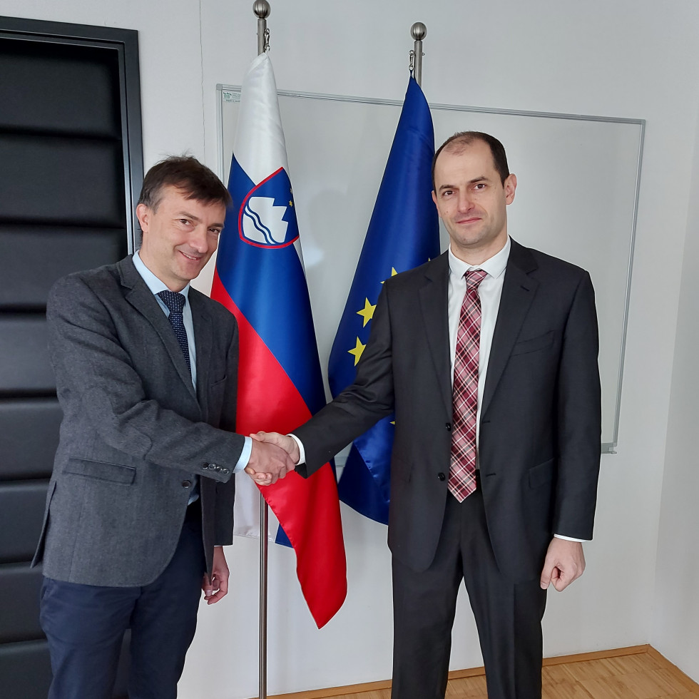 Rokovanje dr. Gašpariča in bolgorskega veleposlanika Bojanova, v ozadju slovenska in evropska zastava. 