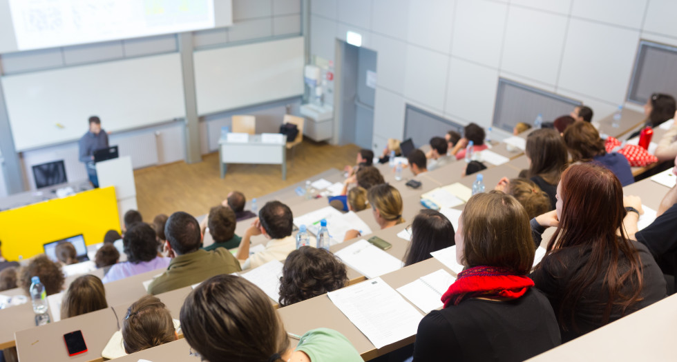 Študentke in študenti v predavalnici spremljajo predavanje profesorja.