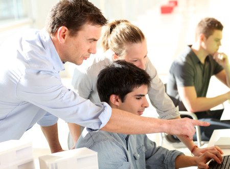 Mentor pomaga dvema mladima sodelavcema pri delu na računalniku.