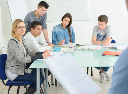 Skupina študentov sedi za mizo in posluša predavatelja.