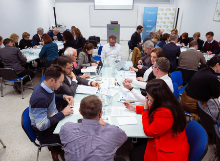 Za mizo sedijo moški in ženske, ki si zapisujejo.