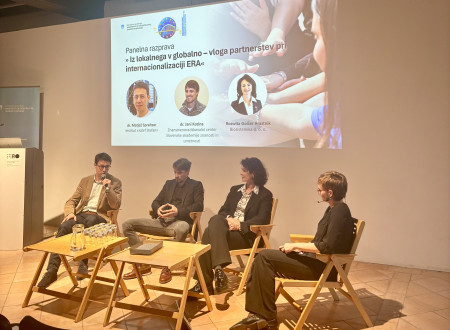 Panelna razprava s štirimi govorci, ki sedijo na odru pred projekcijskim zaslonom z naslovom dogodka