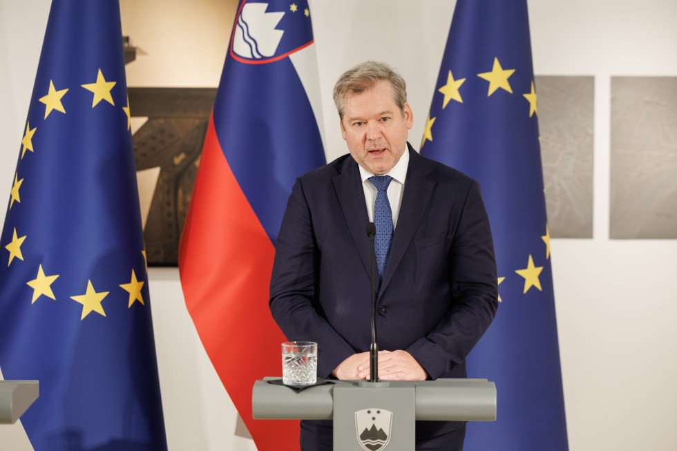 Minister dr. Igor Papič na novinarski konferenci, v ozadju slovenska in evropska zastava.