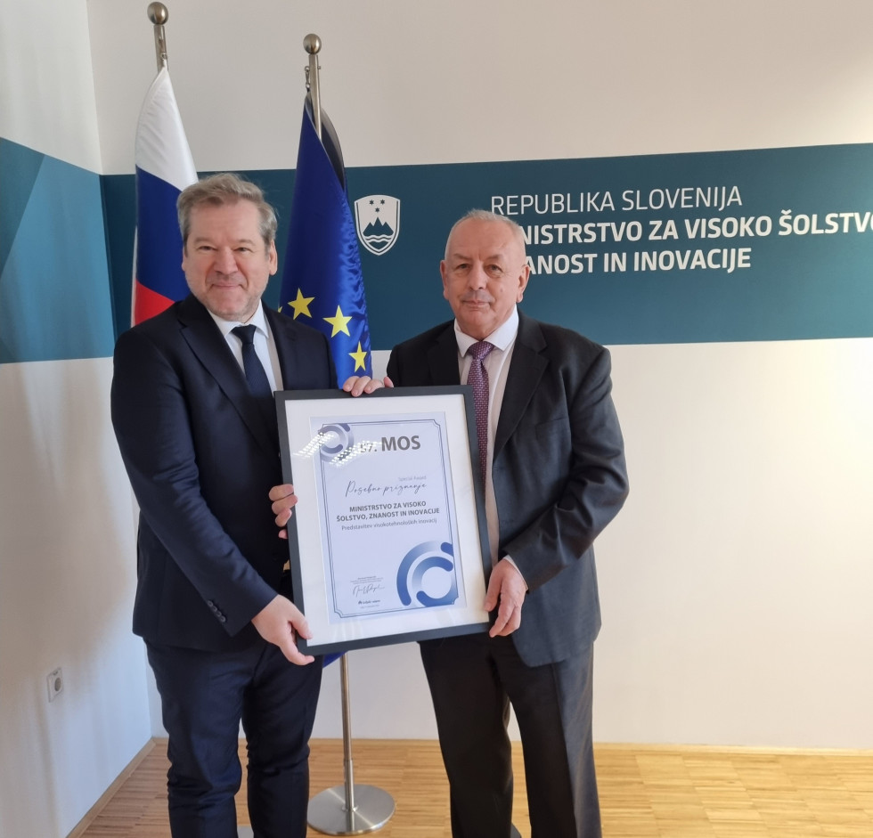 Minister Papič in gospod Škrlec skupaj držita priznanje. V ozadju slovenska in evropska zastava.
