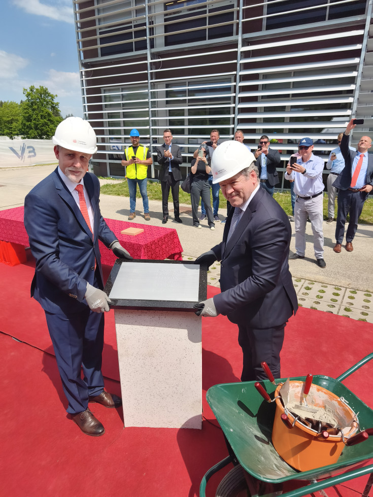 Ceremonialno polaganje temeljnega kamna: Rektor in minister s čeladama držita spominsko ploščo ob podstavku.