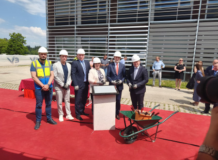Slavnosti gostje v zaščitnih čeladah ob temeljni plošči na gradbišču.